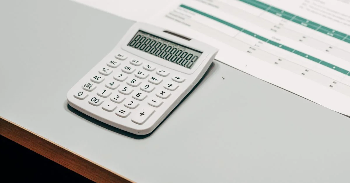 Gros plan d'une calculatrice blanche à côté d'un tableur financier sur un bureau.
