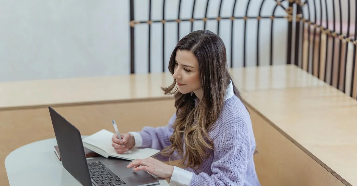 Une jeune femme se concentrant sur son travail avec un ordinateur portable et un cahier dans un cadre intérieur moderne.