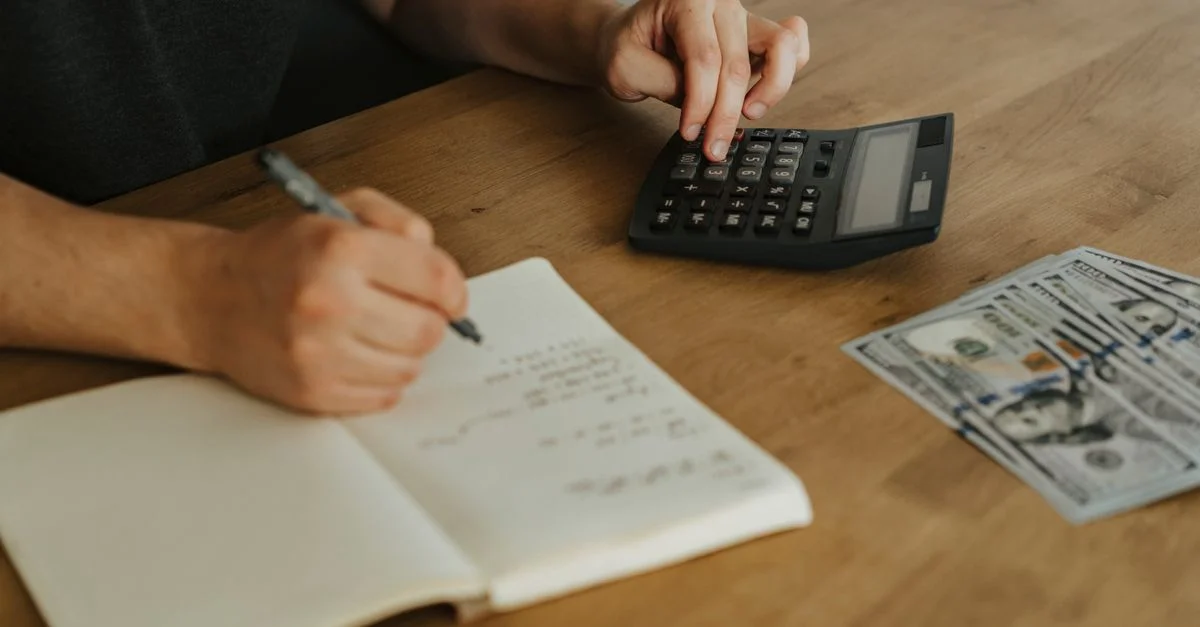 Gros plan sur des mains utilisant une calculatrice avec un carnet et de l'argent sur une table en bois.