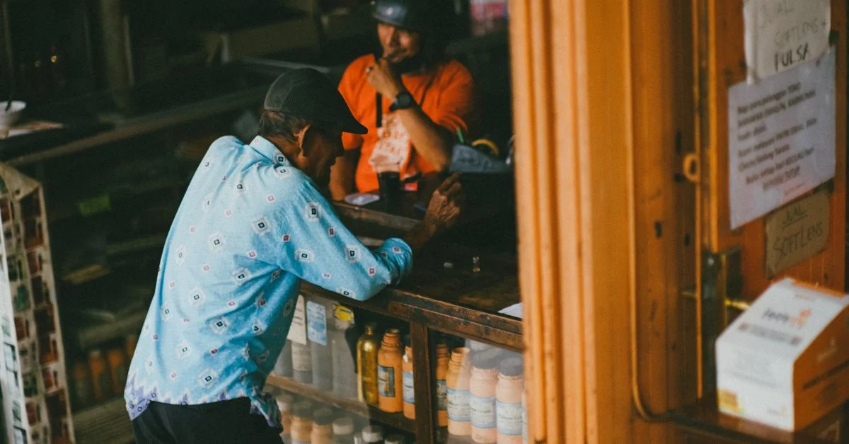 Un homme âgé portant une chemise bleue discute avec un commerçant au comptoir d'un magasin local.